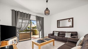 A modern living room with a flat-screen TV, a wooden coffee table, a leather sofa, and a large window with curtains. - Coastal Charm Apartment (Lagos)