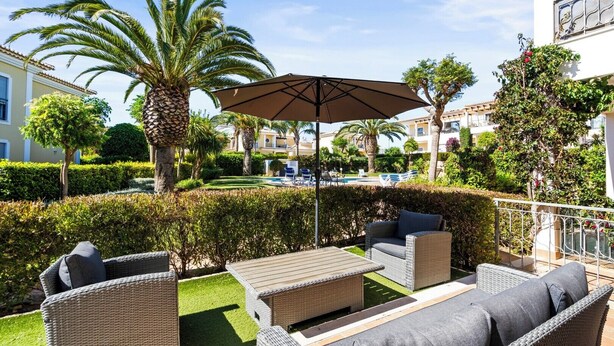 A patio area with wicker furniture, a large umbrella, and a pool in the background. - Coastal Charm Apartment (Lagos)