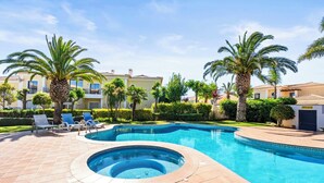 A swimming pool with a hot tub, surrounded by palm trees and lounge chairs, with buildings in the background. - Coastal Charm Apartment (Lagos)