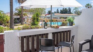 Ein Balkon mit einem weißen Sonnenschirm, einer Champagnerflasche, einem Glas und einem Teller Essen.