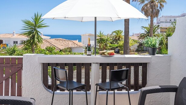 Eine Terrasse mit zwei schwarzen Stühlen, einem weißen Sonnenschirm und einer Champagnerflasche.