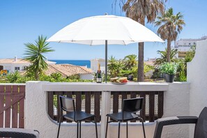 Eine Terrasse mit zwei schwarzen Stühlen, einem weißen Sonnenschirm und einer Champagnerflasche.