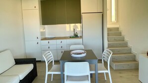 Ein kompakter Wohnbereich mit Küchenzeile, einem Essbereich mit Tisch und Stühlen, einer Couch und einer Treppe, die in einen oberen Bereich führt.