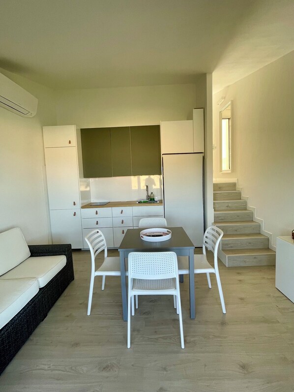 A compact living space with a kitchenette, a dining area with a table and chairs, a sofa, and a staircase leading to an upper level.