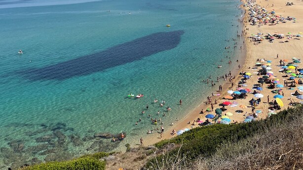 Ein Strand mit klarem türkisfarbenem Wasser, einem Sandufer und ein paar Booten in der Ferne.