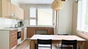 A kitchen with wooden cabinets, a white countertop, a dining table with chairs, and a hanging light fixture.