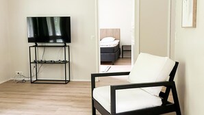 A room with a black TV stand, a white chair, and a bed in the background.