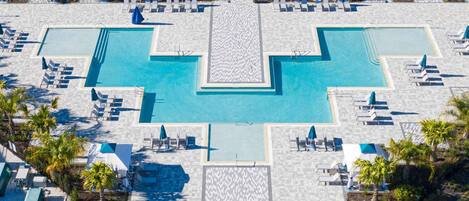 An aerial view of a resort with multiple swimming pools, sun loungers, and palm trees.