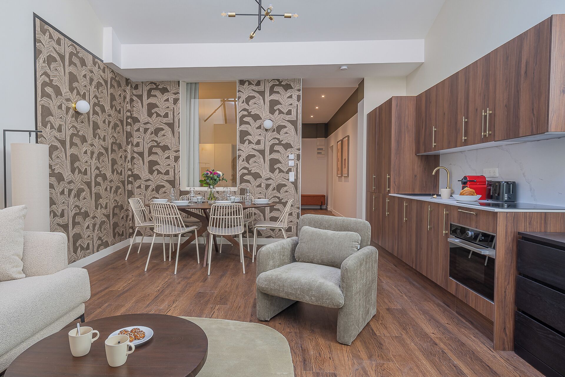 A modern living room with a dining area, wooden flooring, and a kitchen with built-in appliances.