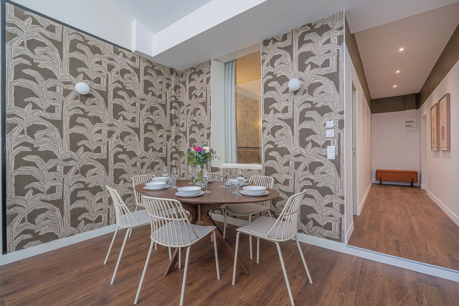 A dining area with a round table, white chairs, and a patterned wallpaper.