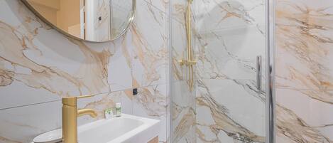 A bathroom with a marble backsplash, a gold showerhead, and a white sink.