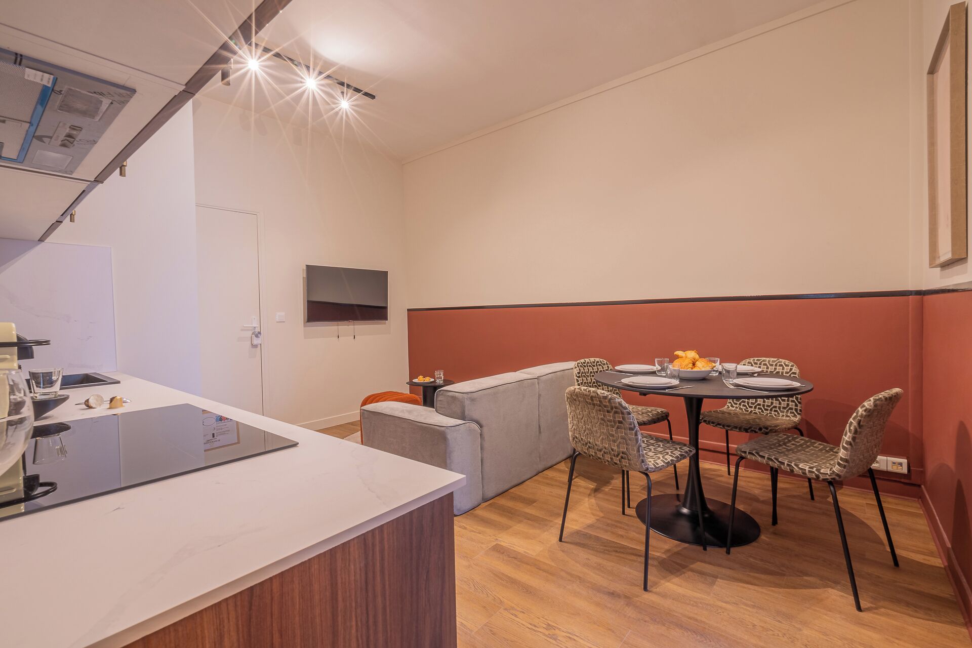 Et moderne køkken med en hvid bordplade, indbygget ovn og mikroovn. Spiseområde med et rundt bord og mønstrede stole.