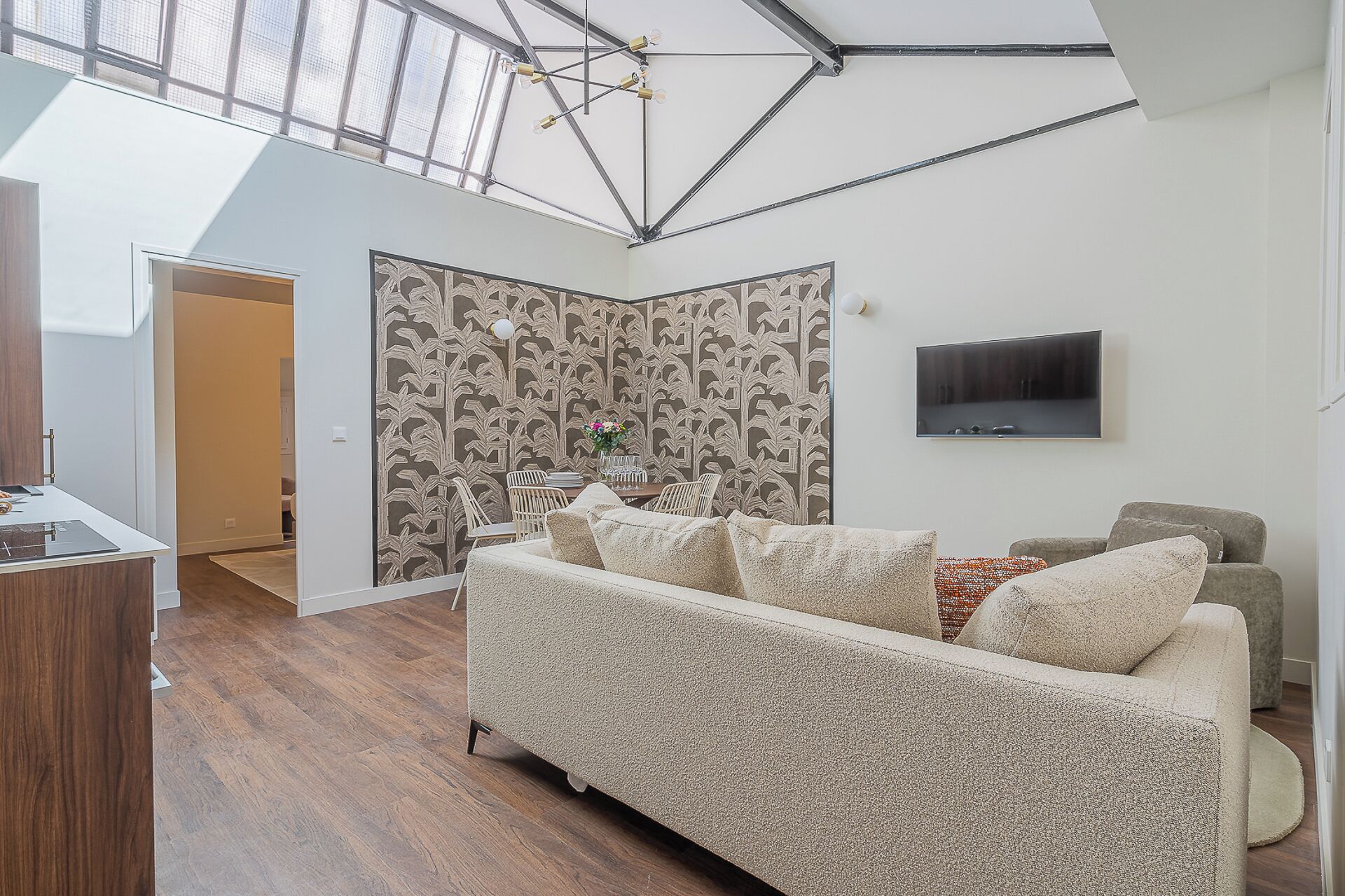 A modern living room with a high ceiling, a large sofa, a TV, and a patterned wallpaper.
