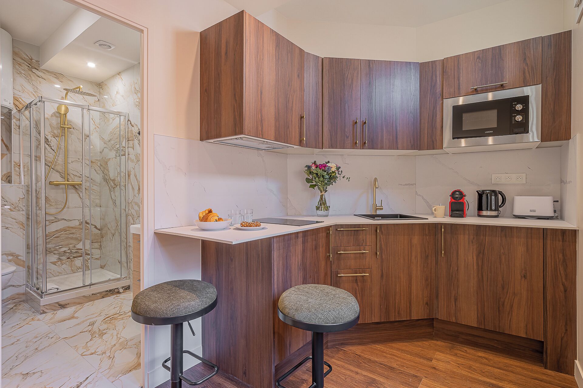 A modern kitchen with wooden cabinets, a built-in microwave, and a glass shower enclosure.