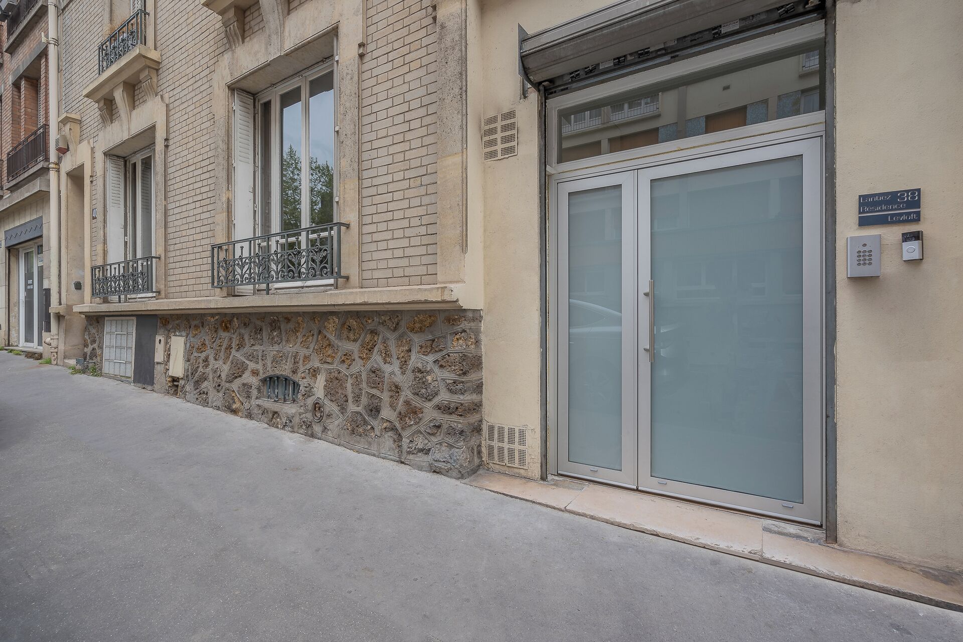 Un edificio con fachada de piedra, un balcón de metal y una puerta de cristal grande con cerradura numérica.