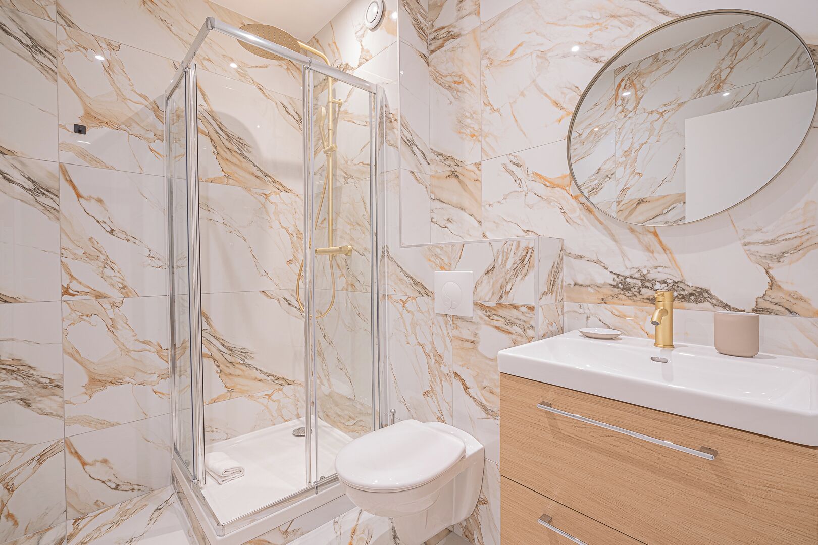 Une salle de bain dotée d’une douche à parois de verre, de toilettes, d’un lavabo avec un robinet doré et d’un mur décoré d’un motif marbré.