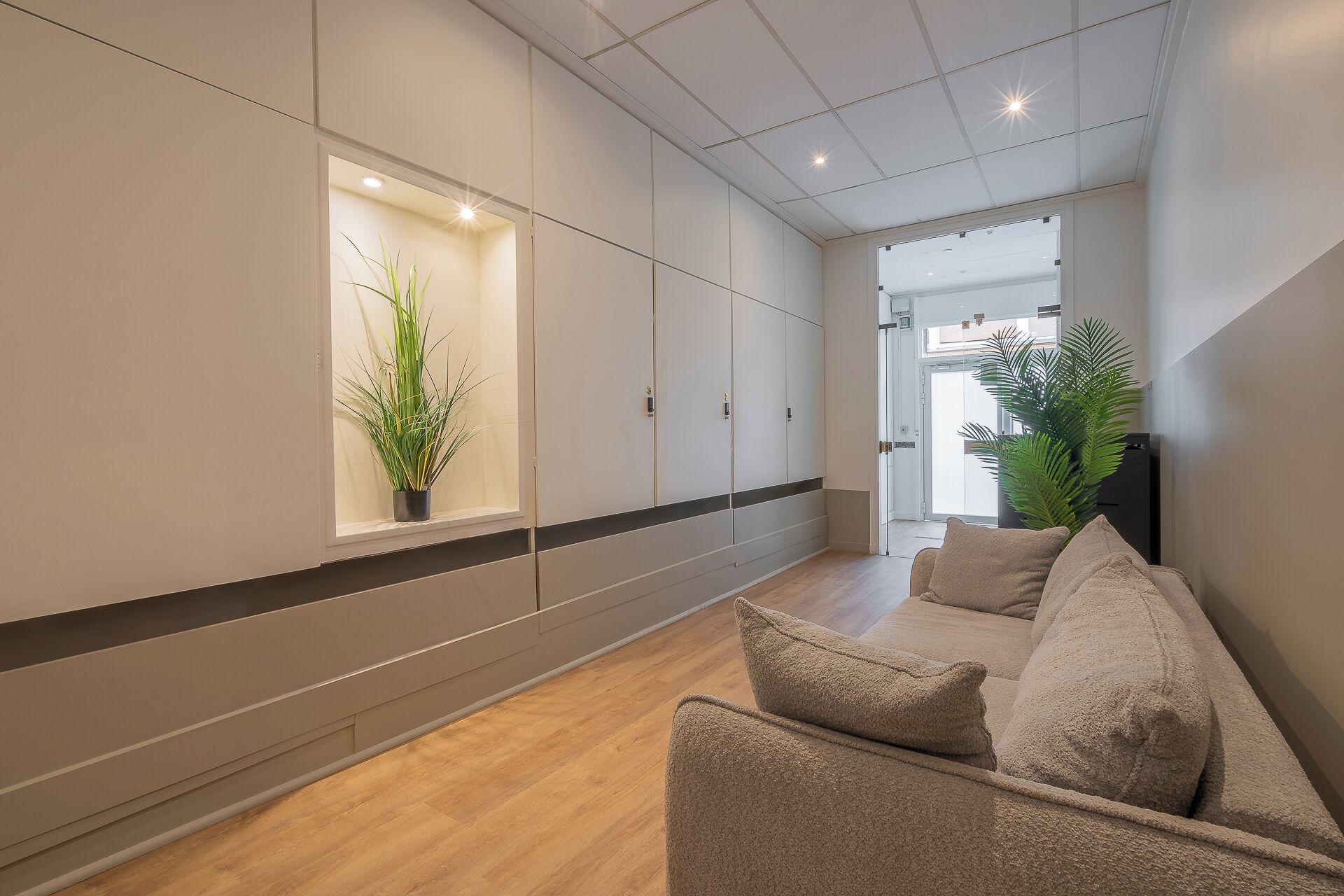 A modern hallway with a sofa, potted plants, and a large window.