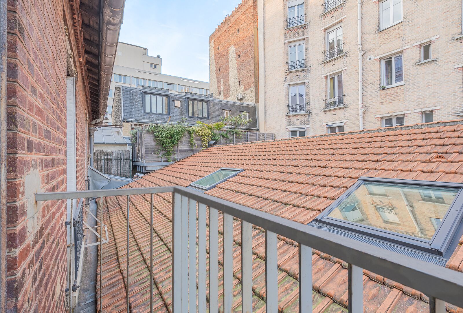 Une terrasse sur le toit, avec un toit en tuiles, une rambarde en métal et une vue sur les bâtiments adjacents.