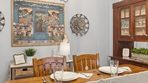A dining room with a wooden table set for two, surrounded by chairs. There is a decorative painting above the table, a clock on the wall, and a cabinet with glass doors to the right. - Private Hot - Private Yards - WIFI (Fredericksburg)