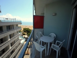 Ein Balkon mit Blick auf den Strand, weiße Plastikstühle und ein rotes Objekt an der Wand.