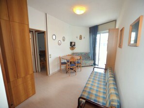 A compact room with a bed, a small table with chairs, a sofa, and a television on the wall. - Seaside Bliss Apartment With sea View (Lignano Sabbiadoro)
