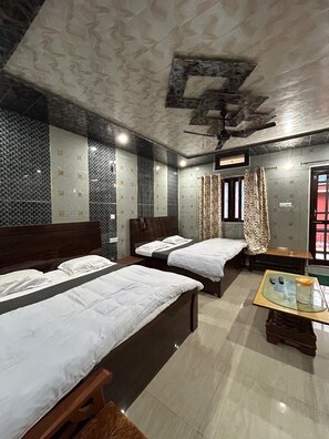 Quarto de hotel com duas camas, uma mesinha com tampo de vidro e um ventilador de teto.