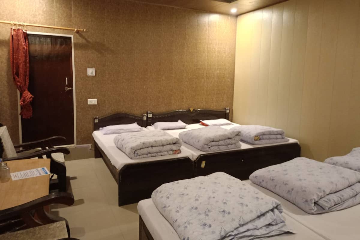 A hotel room with a large bed, two smaller beds, a wooden desk, and a wardrobe.