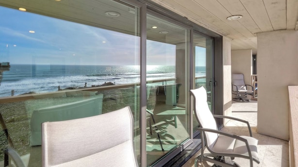 Een balkon met uitzicht op de oceaan, glazen deuren en twee witte stoelen.