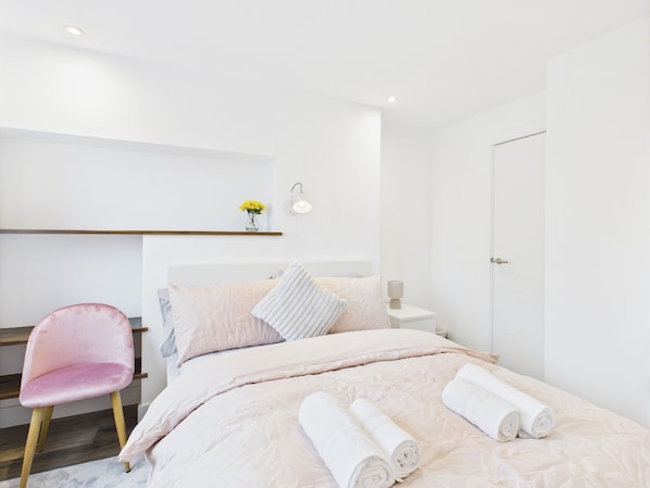 A modern hotel room with a bed, a chair, a nightstand, and a wall-mounted shelf with flowers.
