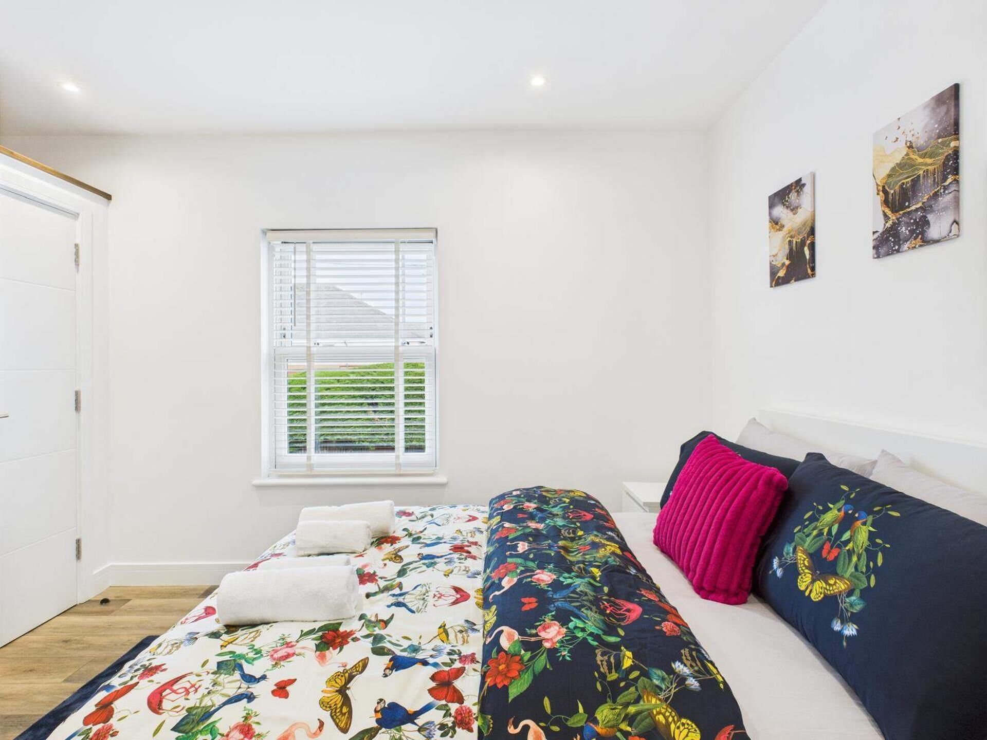 A bedroom with a bed, pillows, a window, and artwork on the wall.