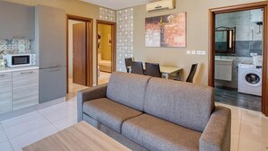 A modern apartment with a kitchenette, a grey sofa, a dining area, and a laundry room.