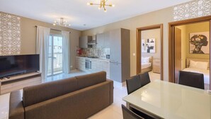 A modern living room with a sofa, a TV, and a dining area with a glass table.