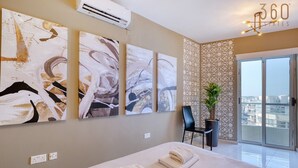 A hotel room with a bed, artwork on the wall, a chair, a potted plant, and a view of the city.