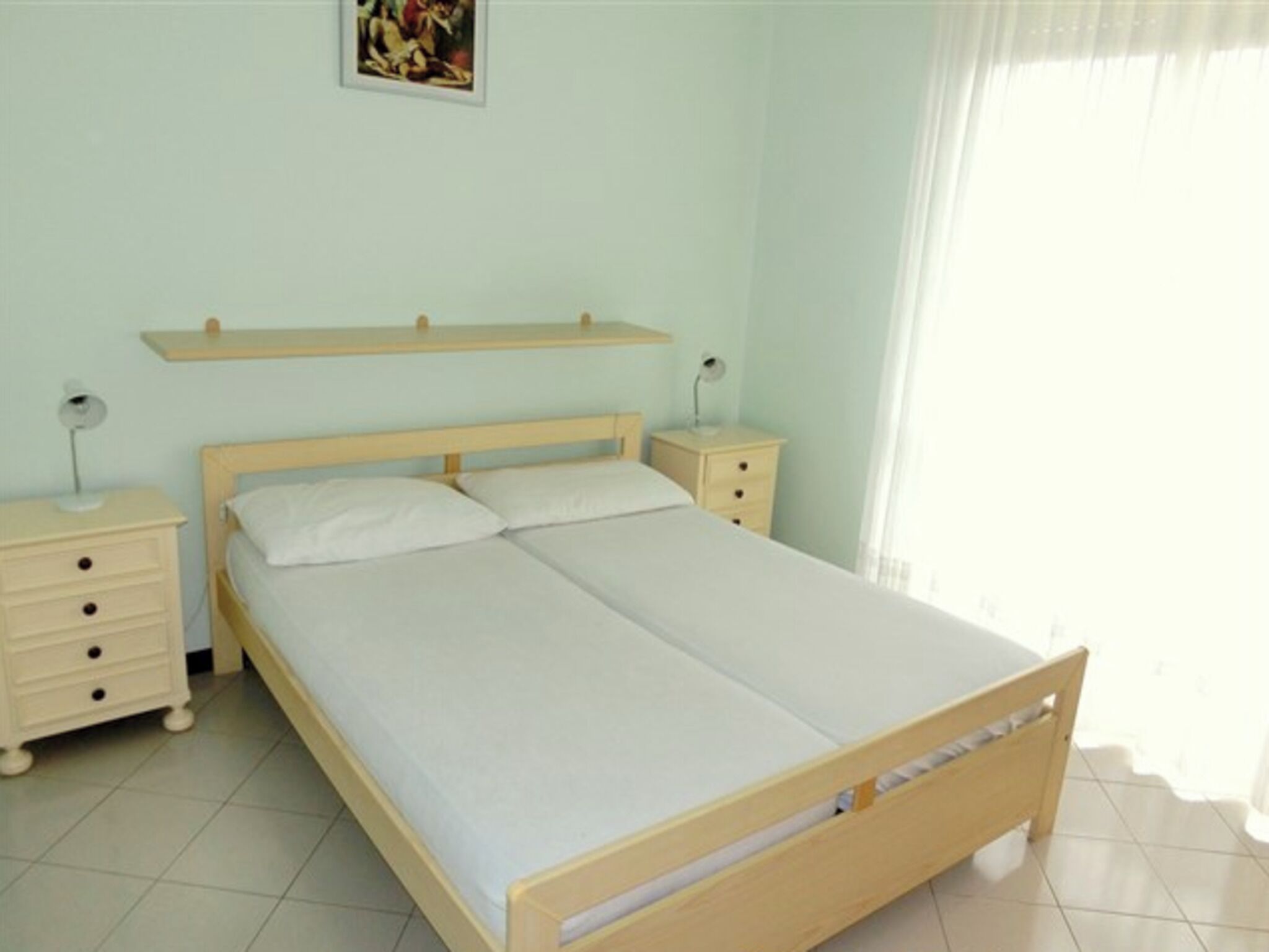Een slaapkamer met een houten bed, twee nachtkastjes, een nachtkastje, een wandplank en een enkele wandlamp.