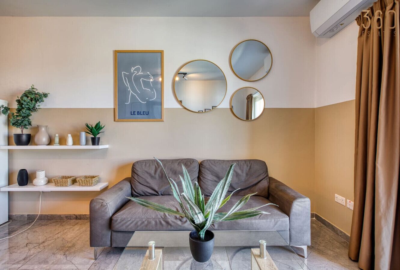 Una sala moderna con un sofá gris, una planta en maceta y espejos decorativos en la pared.