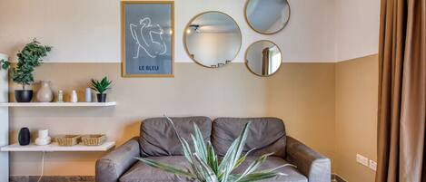 Una sala moderna con un sofá gris, una planta en maceta y espejos decorativos en la pared.