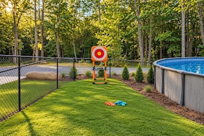 A fenced backyard with a target, a swimming pool, and a grassy area. - Woodland Aster | Secluded Stay with Pool and Sauna (Menlo)