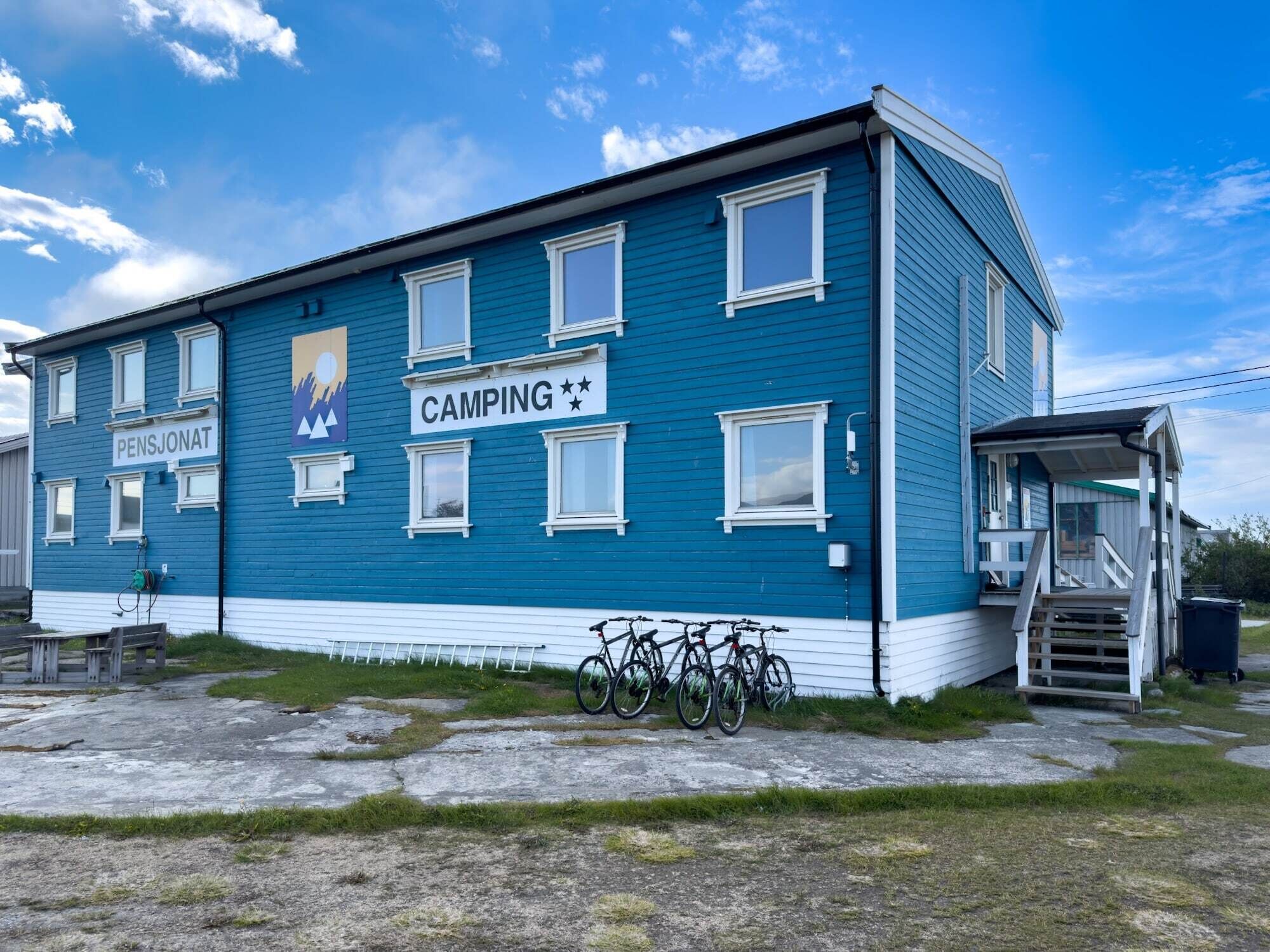 Un bâtiment bleu avec une enseigne indiquant « CAMPING » et « PENSJONAT », ce qui signifie qu’il s’agit d’un établissement proposant des emplacements de camping et des hébergements.