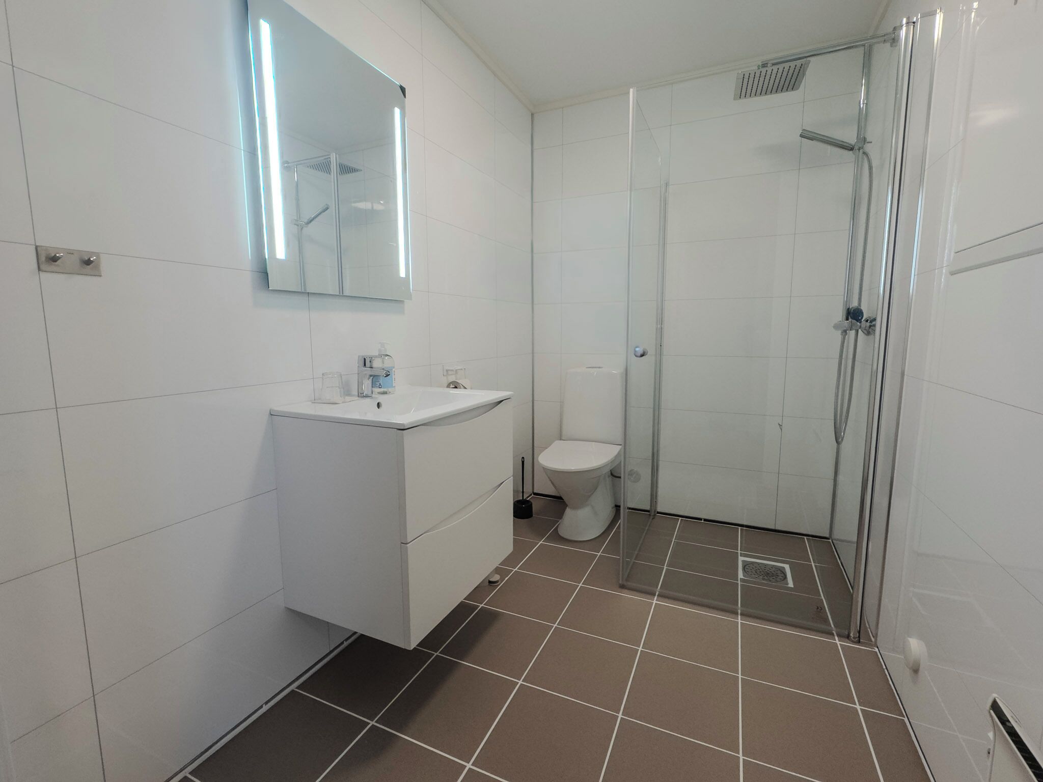 A bathroom with white tiles, a sink, a toilet, and a glass-enclosed shower area.