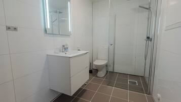 A bathroom with white tiles, a sink, a toilet, and a glass-enclosed shower area.