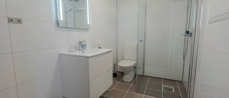 A bathroom with white tiles, a sink, a toilet, and a glass-enclosed shower area.