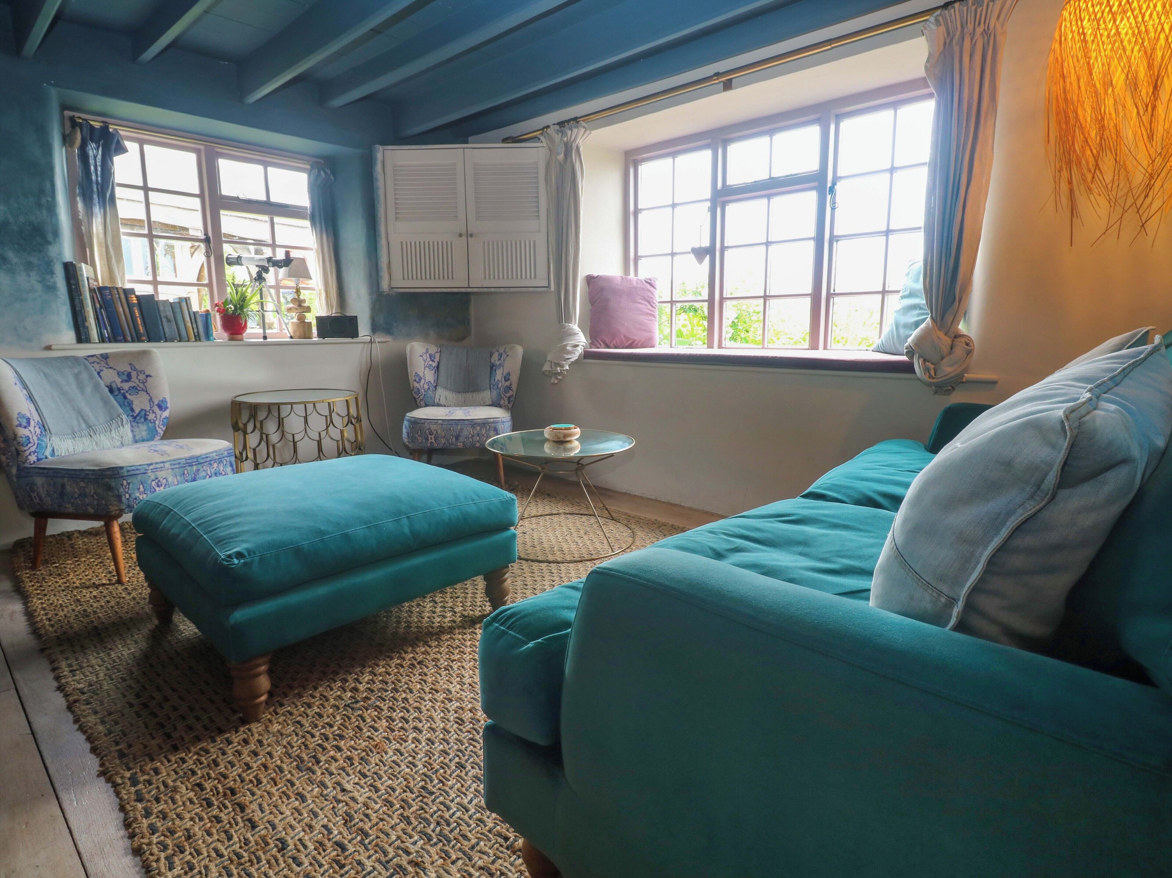 Un salon chaleureux avec des meubles de couleur turquoise, un tapis à motifs et une bibliothèque remplie de livres et d’objets décoratifs.
