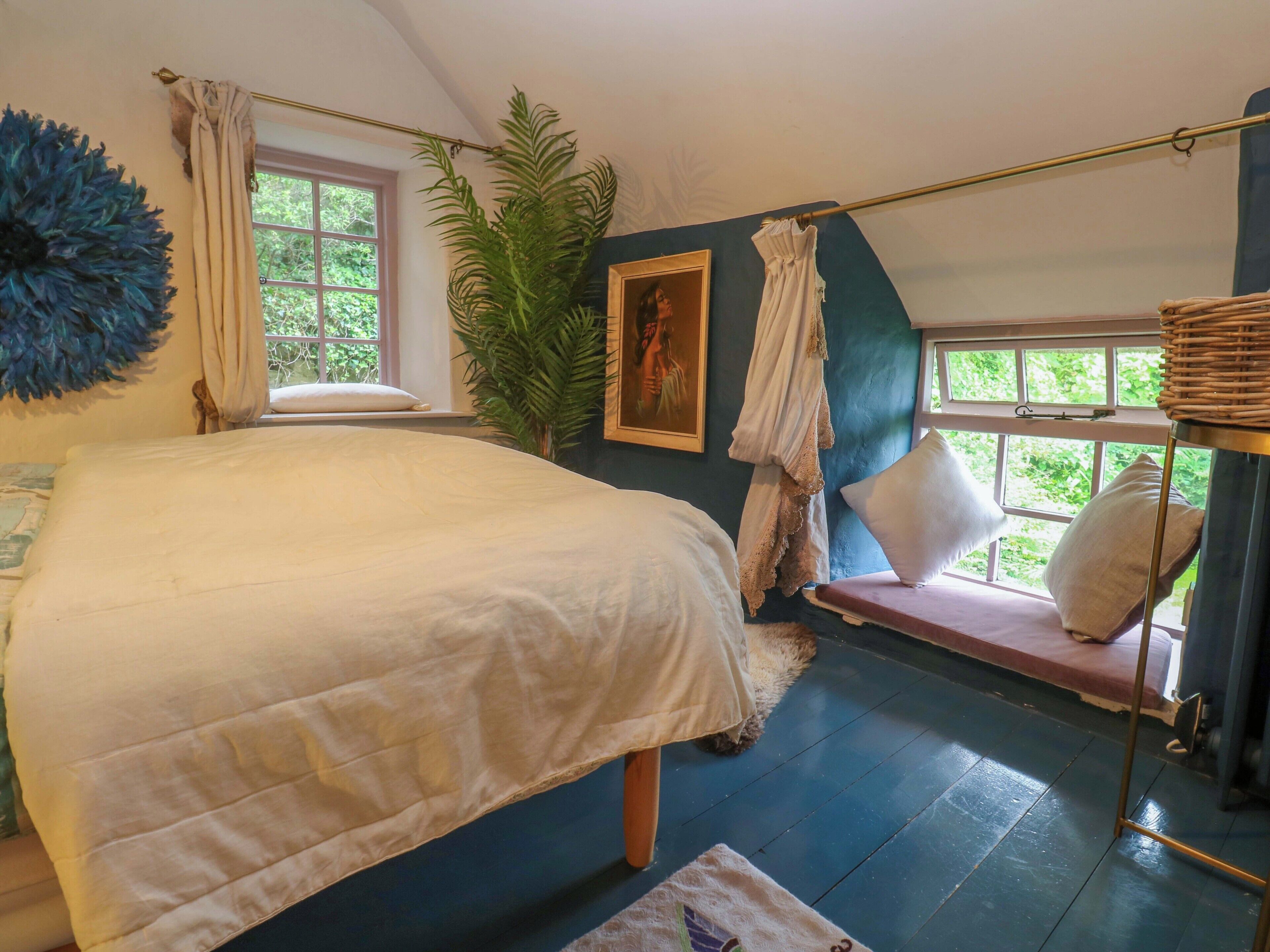 Quarto com uma cama grande, janela com cortinas, planta em vaso e um quadro na parede.