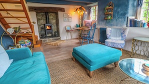 Una sala de estar acogedora con chimenea de piedra, un sofá azul, una escalera de madera y una estantería.