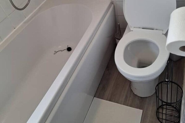 A bathroom with a bathtub, toilet, and a small trash bin.