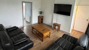 A living room with a wooden coffee table, black leather sofas, a TV mounted on the wall, and a door leading to another room. - 3 Bed House Sleeps 5 - Free Parking - Tv & Wifi (Sheffield)