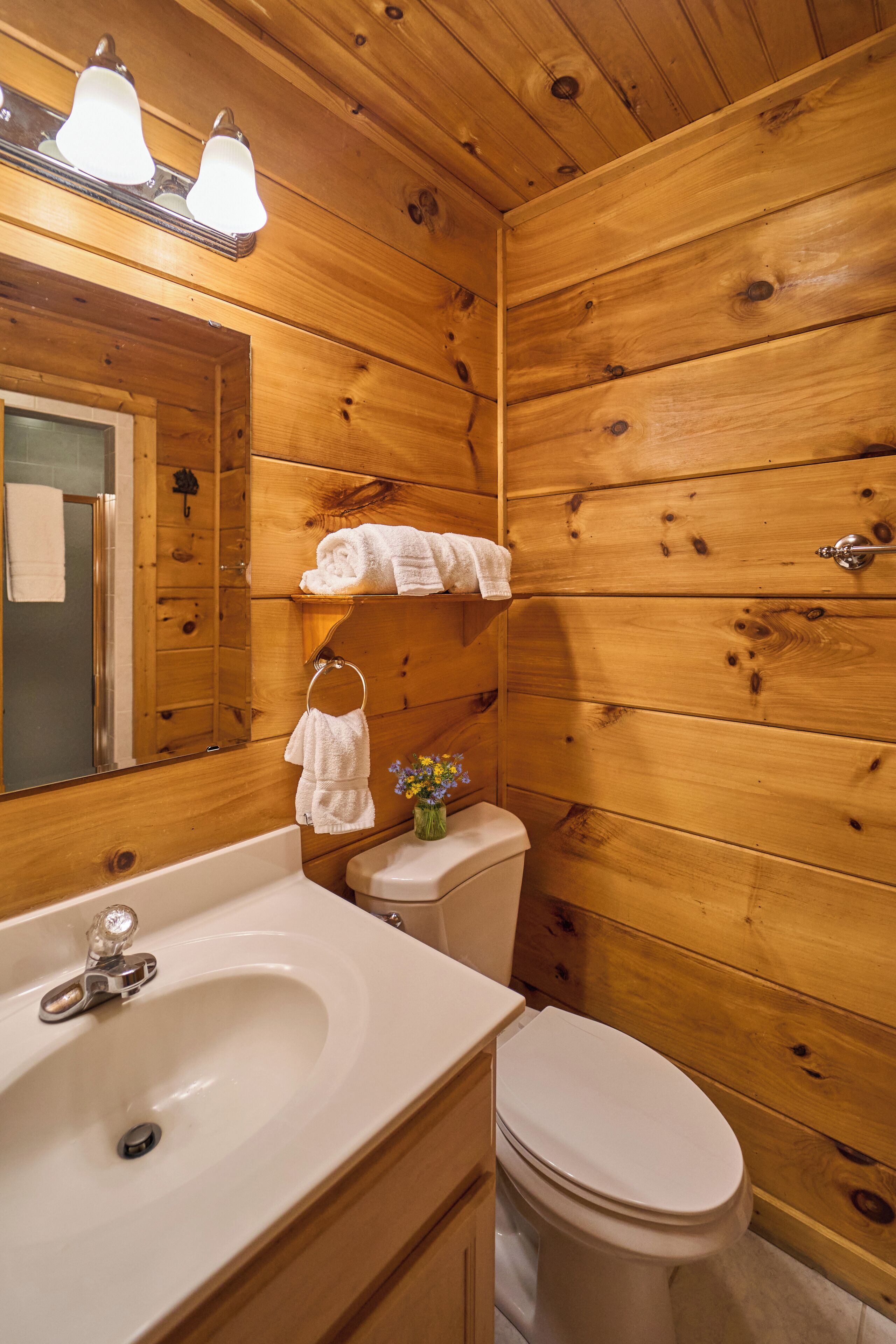 A wooden bathroom with a white sink, mirror, and toilet.