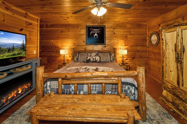 A wooden cabin room with a bed, a television, and a fireplace.