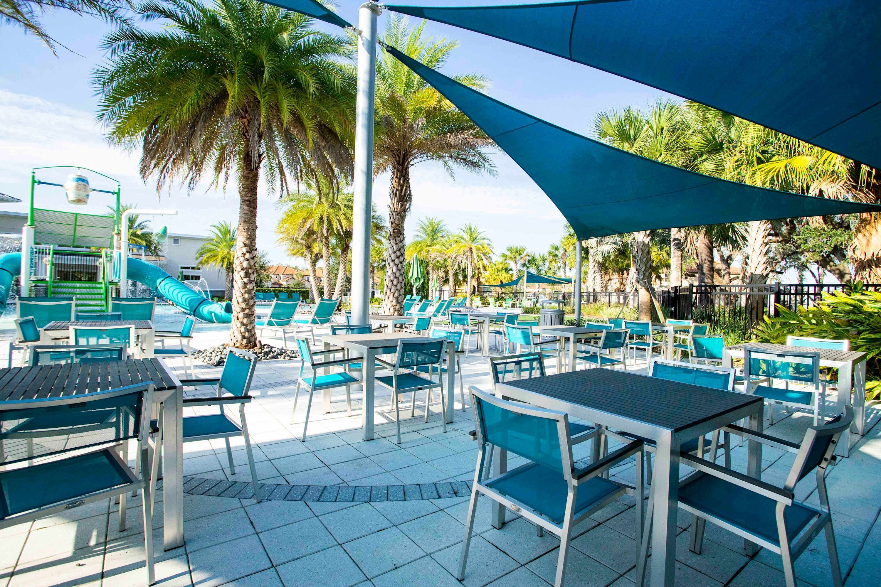 Un espace extérieur avec une piscine, des chaises longues et des tables, des palmiers et un toboggan aquatique.