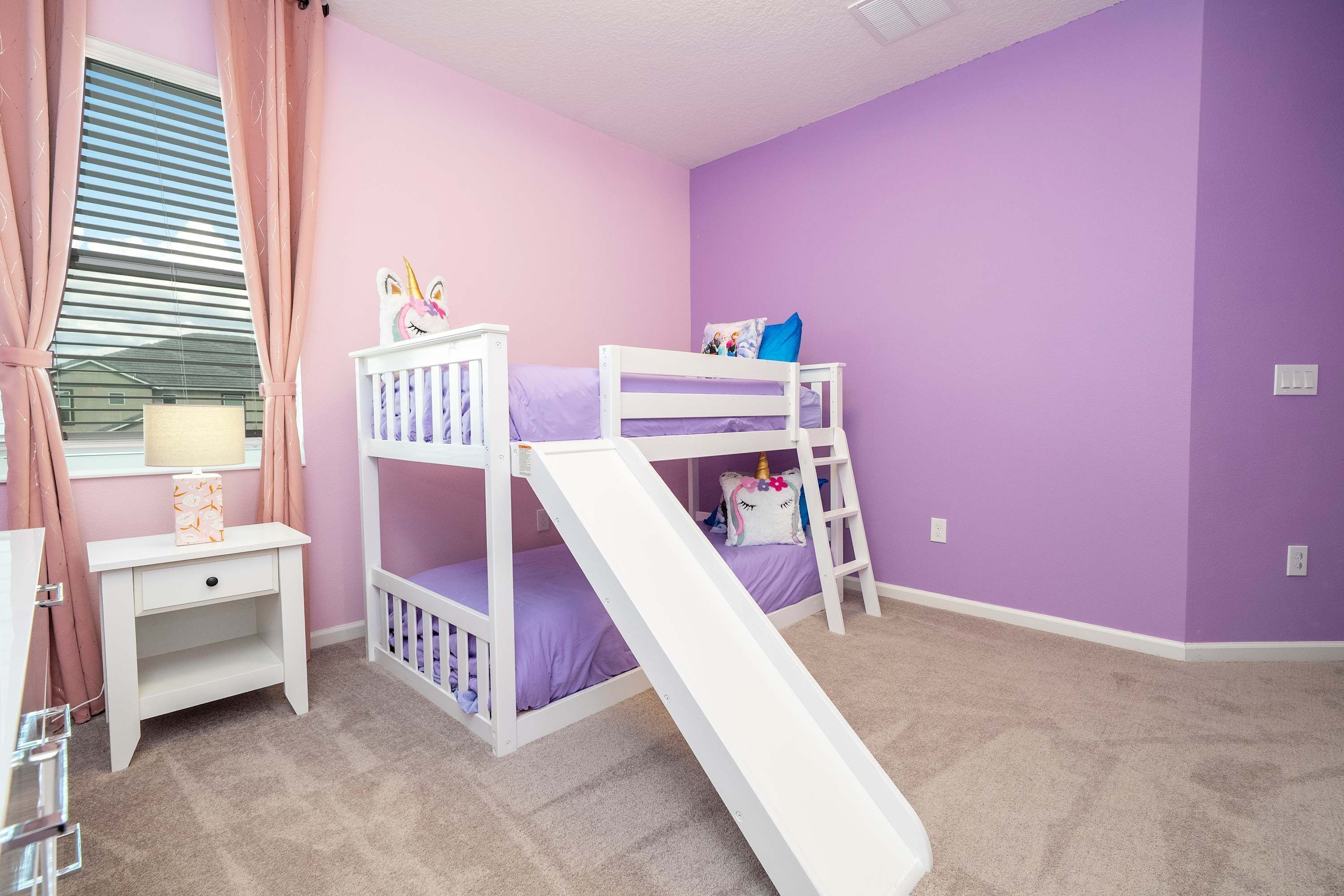 A child's bedroom with bunk beds, a slide, a nightstand, and a window with curtains.